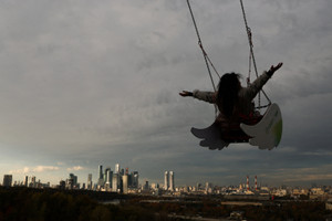 A woman rides a swing as the Moscow International Business Centre rises in the background, at an autumn day in Moscow