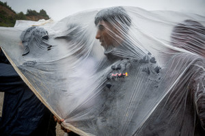 Migrants shield themselves from the rain while queuing to charge their mobile phones at an NGO stand in Ceuta.
