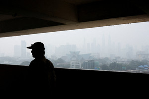 A man walks along a corridor in a residential building with Kuala Lumpur's skyline shrouded in haze from wildfires in Indonesia in the background, in Kuala Lumpur
