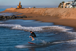Skimboarder walks by a sand berm on Newport Beach