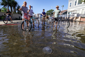 People bike through a flooded street in Newport Beach, California