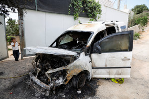 Palestinians stand near destroyed cars, which Palestinians say were burned by Israeli settlers, in Aqraba