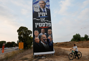 A man on a bicycle looks at a vandalised pre-election campaign billboard for the Likud party, at the entrance to the city of Netivot