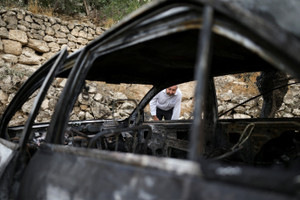 A Palestinian inspects a damaged car, which Palestinians say was burned by Israeli settlers, in Mukhmas