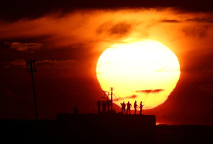 People fish off the harbour wall at sunrise during warm Autumn weather, in Hastings